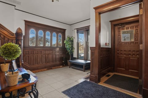 Interior view of a stylish entrance with wood paneling and stained glass windows, featuring a bench and decorative plants.