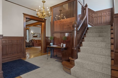 Elegant entrance featuring wood paneling, chandelier, and staircase.