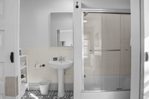 Modern bathroom featuring a glass shower, patterned flooring, and a sleek pedestal sink.
