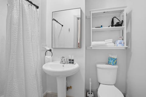 Modern bathroom with a shower curtain, clean sink, and organized shelves displaying towels and toiletries.