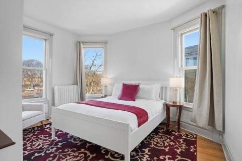 Inviting bedroom featuring a white bed, burgundy accents, and large windows.