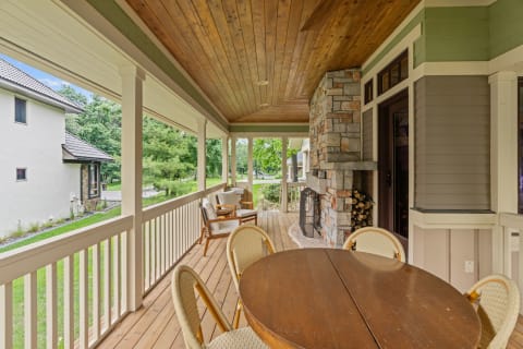 Outdoor porch with wooden ceiling, stone fireplace, and dining table surrounded by wicker chairs.