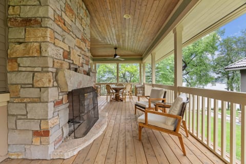 A cozy porch featuring a stone fireplace, wooden ceiling, and outdoor dining area with a view of the green surroundings.