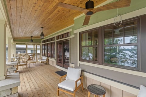 A beautifully designed porch featuring wooden ceilings, dark-framed windows, and comfortable seating.