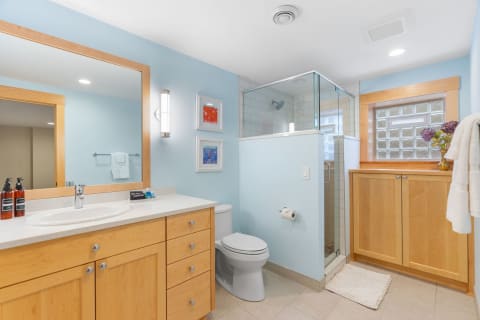 Modern bathroom with light blue walls, wooden cabinets, and a glass shower enclosure.