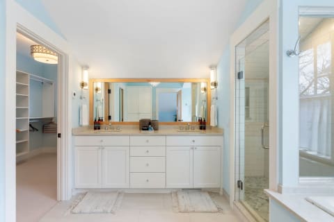 Modern bathroom showing a dual-sink vanity, large mirror, and a glass shower enclosure.