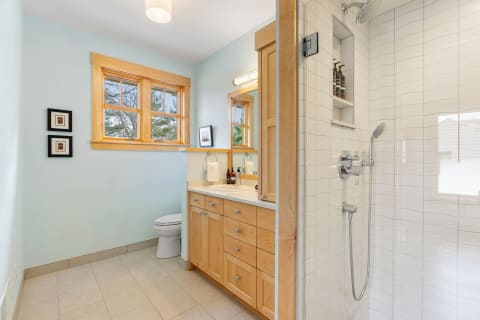 Modern bathroom with light blue walls, wooden vanity, and shower.