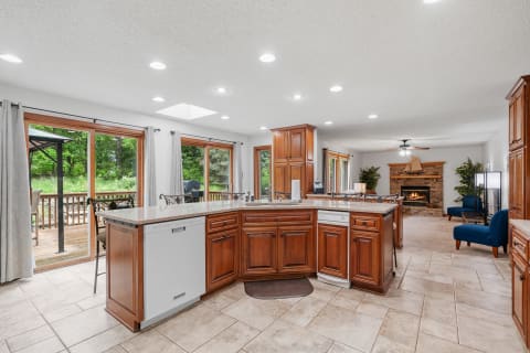 Spacious kitchen with wooden cabinetry, granite countertops, and a view of lush greenery through large windows.