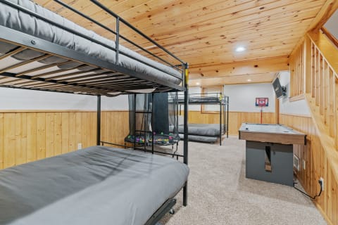 Spacious basement room featuring bunk beds, an air hockey table, and a mounted TV.