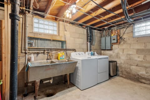 Basement laundry room featuring washing machines, a utility sink, and exposed pipes.
