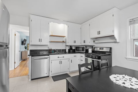 A bright kitchen featuring white cabinets, a black gas stove, and a black dining table.