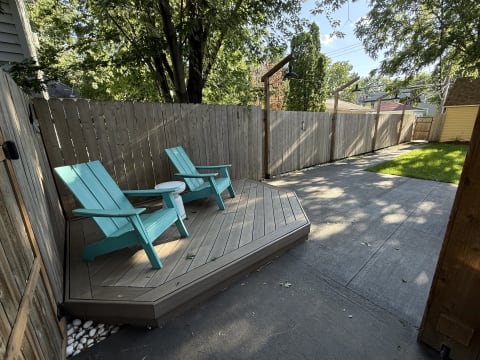 A serene backyard with two aqua blue chairs on a wooden deck, surrounded by a wooden fence and green grass.