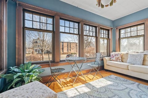 Cozy sunroom with wooden windows, a beige couch, and a small table with chairs.