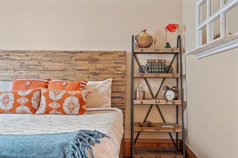 A cozy bedroom featuring a wooden headboard, decorative pillows, and an industrial-style shelf.