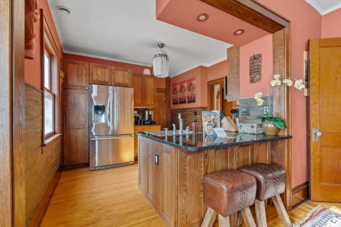 A modern kitchen featuring wooden cabinets, stainless steel fridge, and dark granite countertops.