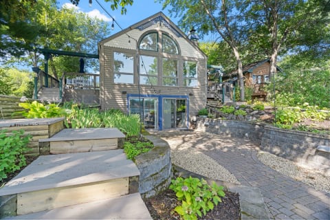 A modern cabin with large windows and a wooden staircase, set in a green landscape.