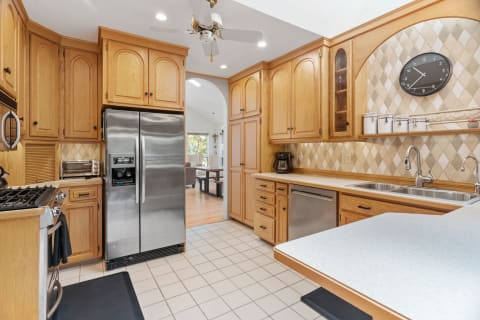 A kitchen with oak cabinets, stainless steel refrigerator, and double sink.