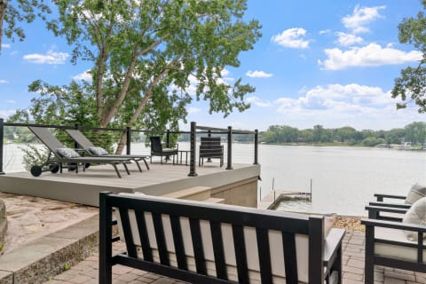 A serene lakeside deck featuring reclining chairs and a table, surrounded by trees and water.