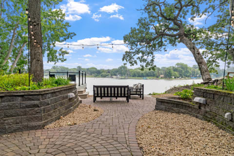 Outdoor seating area by a lake with beautiful landscaping and blue sky.