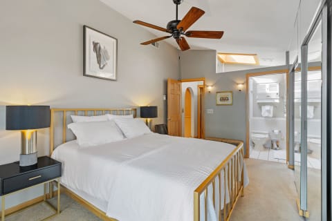 A stylish bedroom featuring a golden bed frame, white bedding, and contemporary bedside tables with lamps.