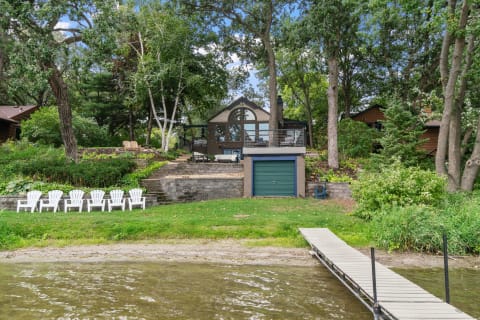 Serene lakeside view featuring a modern house and white Adirondack chairs.
