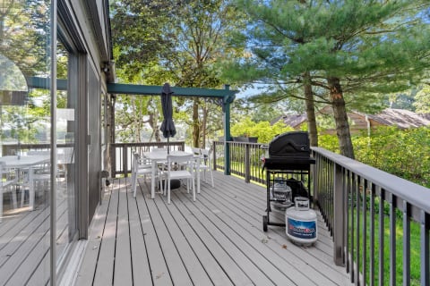 Outdoor deck with a dining table, chairs, and a grill, embraced by greenery.