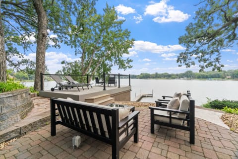Outdoor seating area by a lakeside with trees and a dock.
