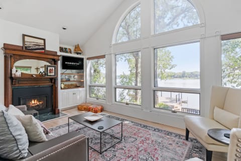 A spacious living room with large windows overlooking a lake, featuring a fireplace and cozy seating.