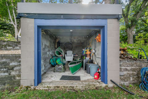 Outdoor storage shed with a canoe and gardening tools.