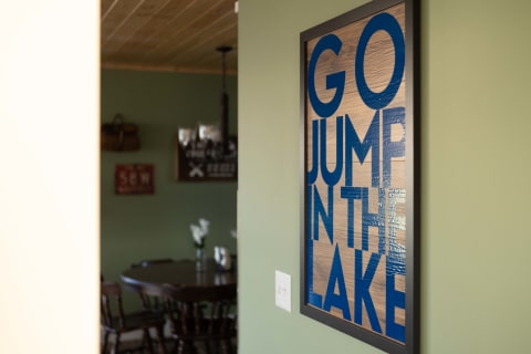 Framed wall art with the phrase 'GO JUMP IN THE LAKE' in blue letters, set against a light wooden background.