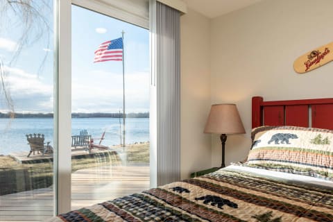 A cozy bedroom featuring a bear-patterned quilt and large sliding doors that open to a view of a lake and a flag.