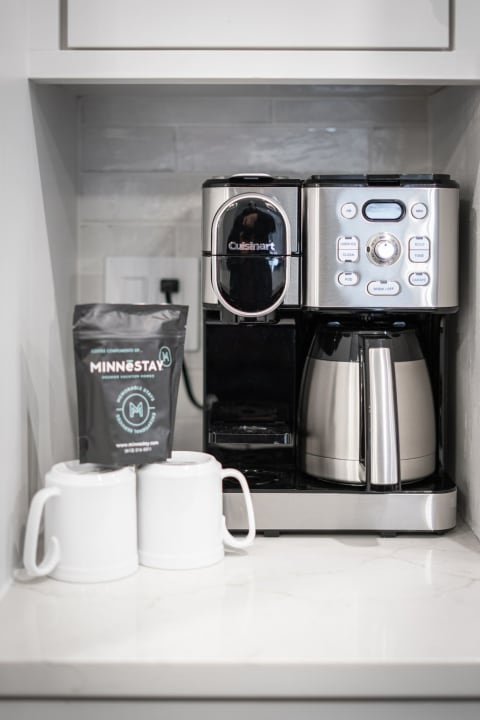 Modern coffee station with a Cuisinart coffee maker, two white mugs, and a bag of coffee.