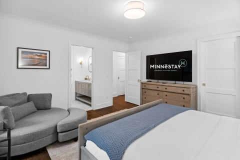 Modern bedroom with grey sectional couch, flat-screen TV, and entrance to a stylish bathroom.