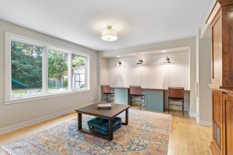 Bright living space with working station, coffee table, and large windows overlooking greenery.