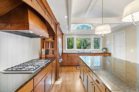 Modern kitchen featuring a large granite island, wooden cabinetry, and spacious windows.
