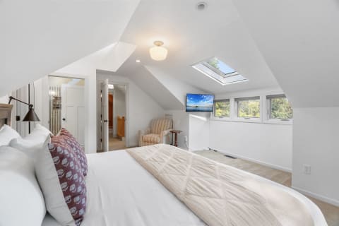 A cozy attic bedroom featuring a bed with white linens, a chair, and a skylight.