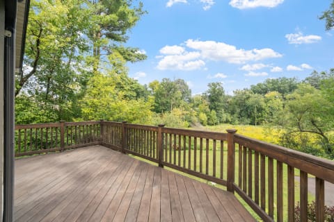 Wooden deck with a view of trees and a field of wildflowers under a blue sky.
