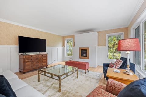 A stylish living room featuring a large TV, elegant furniture, and natural light from windows.