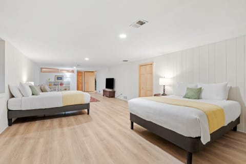 A spacious bedroom with two beds, hardwood flooring, and soft lighting.