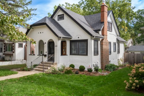 Charming Tudor-style home with brick chimney and manicured gardens in a peaceful residential neighborhood.
