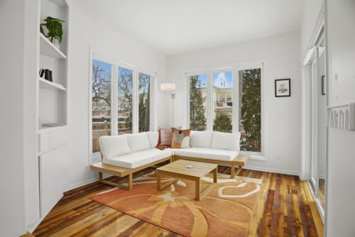 Unwind in your bright corner nook with plush seating and warm wooden floors, where sunlight streams through windows.