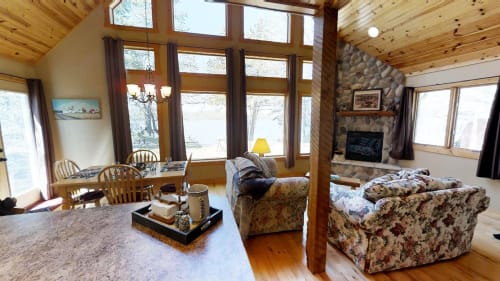 Relax in your cozy living space with soaring wood ceilings, stone fireplace, and panoramic lake views through floor-to-ceiling windows.