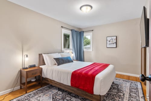 Rest peacefully in your cozy bedroom with crisp linens, warm wood floors, and natural light streaming through blue curtains.